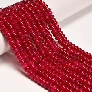May include: Close-up of multiple strands of vibrant red beads. The beads are small, round, and have a glossy finish. The strands are arranged closely together, creating a dense, textured surface. The background is white.