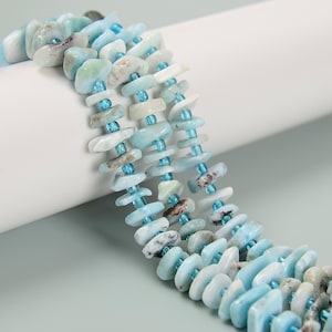 May include: Close-up of a beaded necklace featuring light blue and white irregular-shaped stones. The stones are strung together with small, light blue beads. The necklace is displayed against a white and light blue background.