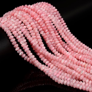 May include: Multiple strands of small, round, light pink beads with a smooth, iridescent finish. The beads are arranged in a dense, cascading cluster, showcasing a consistent soft pink hue and a subtle reflective sheen across their surfaces.