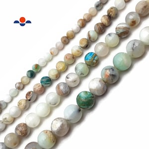 May include: A strand of round, multi-colored gemstone beads. The beads are a mix of green, brown, white, and blue. The beads are strung on a clear thread.