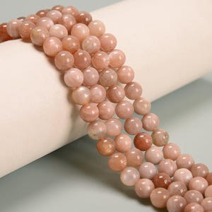 May include: A strand of peach-colored sunstone beads. The beads are round and smooth, and they have a subtle shimmer.