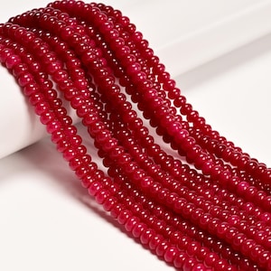 May include: Strands of deep red, round beads. The beads are uniform in size and have a glossy finish. The beads are strung together, creating a flowing, textured appearance. The image is a close-up, highlighting the color and texture of the beads.
