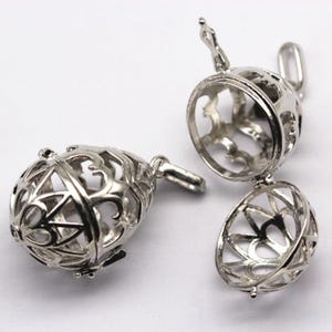 May include: Silver-colored, openwork pendant with a hinged design. The pendant is spherical with intricate, decorative cutouts. One pendant is open, revealing the interior, while another is closed. The pendants have a loop for attaching to a chain.
