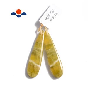 May include: A pair of yellow fluorite earrings with a teardrop shape. The earrings have a light yellow color with white and green stripes. The earrings are hanging from a white tag that says "Yellow Fluorite".