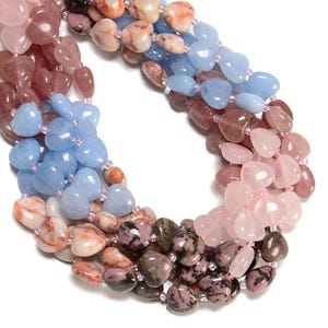 May include: Close-up of a necklace featuring heart-shaped beads in a gradient of colors. The beads transition from pink to blue, with variations of orange, brown, and purple. The beads are strung together with small pink beads.