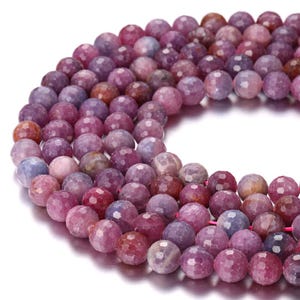 May include: A strand of round, faceted beads in varying shades of purple, magenta, and deep pink. Each bead features a multi-faceted surface that reflects light, creating a textured appearance across the circular arrangement of the gemstone beads.