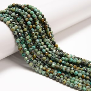 May include: Strands of faceted turquoise beads in varying shades of green, brown, and black. The beads are round and have a sparkling, polished finish. The beads are strung together, creating a flowing, organic shape. Ideal for jewelry making.