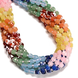 May include: A close-up of a multi-strand necklace featuring a rainbow of faceted gemstone beads. The beads transition through shades of pink, yellow, orange, green, and blue. The necklace is strung on a clear cord, creating a vibrant and colorful accessory.