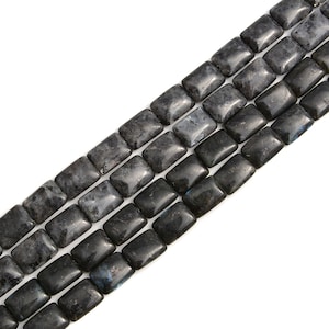 May include: Close-up of strands of rectangular labradorite beads. The beads are a mix of dark gray and black with iridescent blue and gray flashes. The beads are smooth and polished, perfect for jewelry making.