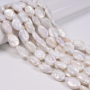 May include: A collection of white, flat, coin-shaped freshwater pearls arranged in multiple strands. Each pearl features a smooth, lustrous surface with subtle iridescent highlights and irregular, organic edges, creating a textured appearance.