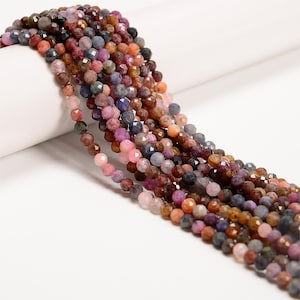 May include: A strand of multi-colored gemstone beads. The beads are faceted and have a variety of shades of pink, purple, blue, and brown. The beads are strung on a clear thread and are ready to be used for jewelry making.