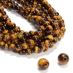 May include: A strand of round, polished tiger's eye beads in shades of brown and gold. The beads are strung on a clear thread and are approximately 8mm in diameter.