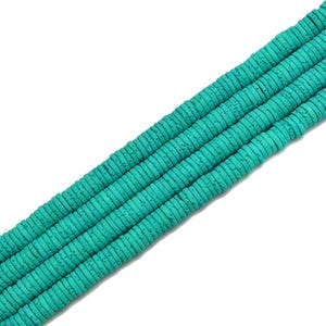 May include: Close-up of several strands of turquoise-colored, flat, round beads. The beads have a textured surface and are strung together, creating a diagonal pattern against a white background. These beads are suitable for jewelry making.