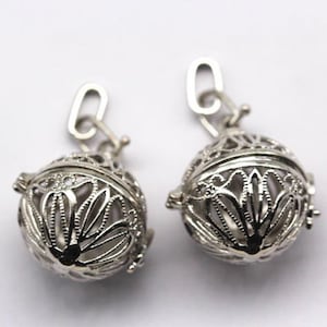 May include: Two silver-colored, filigree-style pendants. Each pendant is a sphere with an openwork design, revealing a lighter interior. The pendants are connected to a small, silver-colored loop at the top.