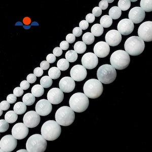 May include: Strands of pale blue-green gemstone beads of varying sizes against a black background. The beads are round and have a smooth, polished appearance. The image is well-lit, highlighting the beads' color and texture. The beads are likely for jewelry making.