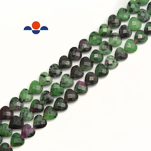 May include: Strands of heart-shaped beads in shades of green and dark red. The beads have a faceted surface, giving them a sparkling appearance. The beads are strung on a red string, perfect for jewelry making.