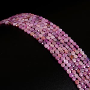 May include: Close-up of strands of faceted, round beads in shades of pink and purple. The beads have a polished, reflective surface and are arranged in a curved pattern against a black background. The beads are likely used for jewelry making.
