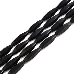 May include: Close-up of several strands of black, faceted gemstone beads. The beads are elongated, with a symmetrical, geometric shape. The beads are strung together, creating a repeating pattern. The background is white.