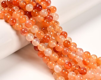May include: Strands of orange and reddish-orange gemstone beads. The beads are round and have a polished, glossy finish. The beads are a mix of opaque and translucent, with variations in color intensity.