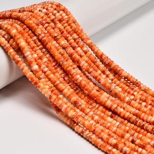 May include: Strands of orange and white gemstone beads. The beads are small, round, and strung together, creating a textured surface. The color is a mix of bright orange and creamy white, with variations in tone throughout the strands.