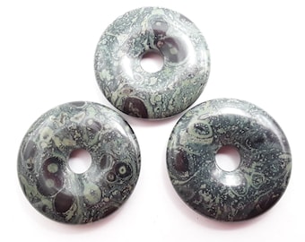 May include: Three round, donut-shaped stones with a hole in the center. The stones have a mottled pattern of dark green, gray, and black. The stones are smooth and polished, and are set against a white background.