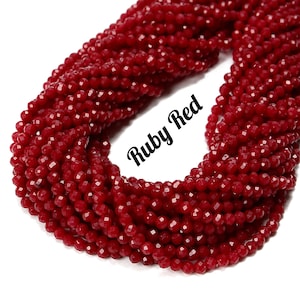 May include: A strand of ruby red faceted glass beads. The beads are small and round, and they are strung together on a clear thread. The beads are arranged in a loose, flowing pattern.