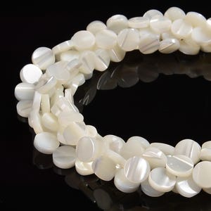 May include: Close-up of a strand of white, disc-shaped beads. The beads have a pearlescent sheen and are strung together, creating a flowing, organic shape. The beads are uniform in size and shape, with a smooth, polished surface.
