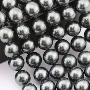 May include: A close-up of a strand of dark gray, lustrous pearls. The pearls are round and evenly sized, reflecting light. The beads are strung together, suggesting they are ready for jewelry making or use in a necklace or bracelet.