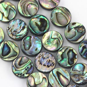 May include: Close-up of a collection of iridescent abalone shell beads. The round beads display a range of colors, including blues, greens, and purples, with a swirling, textured pattern. These beads are ideal for jewelry making.