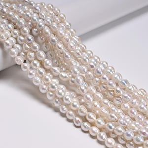 May include: A collection of multiple strands of white freshwater pearls, each featuring an irregular, organic shape with a lustrous, iridescent surface that reflects subtle hints of pink, blue, and cream tones throughout the entire arrangement.