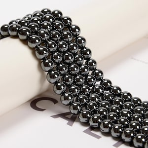 May include: A strand of black hematite beads, each bead is round and smooth. The beads are strung together on a clear thread.