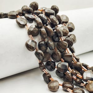 May include: A close-up of a necklace featuring faceted, dark brown gemstone beads. The beads are strung together with copper-colored wire, creating a layered effect. The gemstones have a polished, reflective surface.