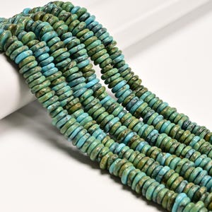May include: Strands of turquoise-colored gemstone beads. The beads are flat, disc-shaped, and vary in shades of blue and green. The beads are strung together, creating a textured and colorful display. The background is white.