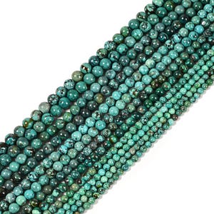 May include: Strands of turquoise beads in various sizes, ranging from small to medium. The beads have a mottled appearance with shades of teal, green, and brown. The beads are arranged diagonally across the frame, creating a visually appealing pattern.