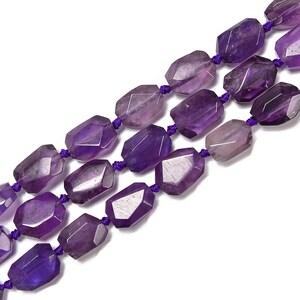 May include: Three strands of faceted amethyst beads, each bead a deep purple hue, are strung on a purple cord. The beads have a geometric shape and are arranged in parallel rows against a white background.