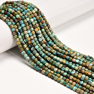 May include: A strand of small, faceted cube-shaped beads in varying shades of turquoise, teal, and brown. Each bead features a unique natural pattern with dark veining and earthy tones, arranged in multiple parallel rows on a string.