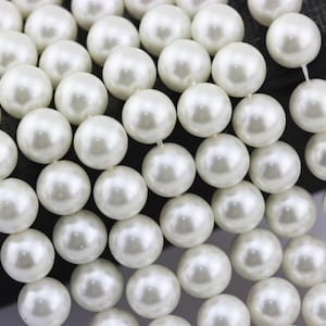 May include: Close-up of a strand of creamy white faux pearls. The pearls are round, smooth, and evenly sized, strung together to create a necklace or bracelet. The image highlights the luster and color of the beads.