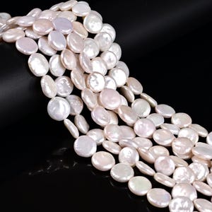 May include: Strands of lustrous, flat, white coin-shaped pearls. The pearls have a subtle iridescent sheen and vary slightly in size. The background is a solid black, highlighting the pearls' natural beauty. Ideal for jewelry making.