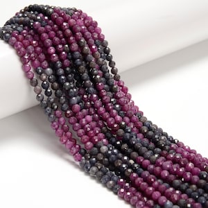 May include: Strands of faceted gemstone beads in shades of deep magenta, purple, and gray. The beads are small and round, with a polished, reflective surface. The beads are strung together, creating a flowing, textured appearance. The gemstones are likely used for jewelry making.