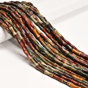 May include: Strands of bamboo-shaped beads in various earthy tones, including red, green, brown, and orange. The beads have a natural, textured appearance and are strung together, creating a visually appealing pattern. The beads are likely used for jewelry making.