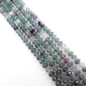 May include: Strands of faceted beads in shades of green, purple, and clear. The beads are strung together, creating a diagonal pattern across the frame. The beads have a sparkling, polished appearance, suggesting they are made of a gemstone or crystal.