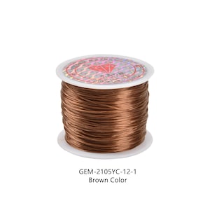 May include: A spool of brown elastic cord, labeled "GEM-2105YC-12-1 Brown Color." The cord is tightly wound on a white plastic spool with a holographic label on top. The cord appears to be made of a stretchy material.