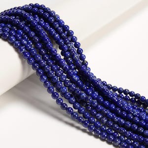 May include: Strands of deep blue, round gemstone beads. The beads have a polished, reflective surface and are strung together, creating a flowing, textured appearance. The beads are a rich, dark blue color, with subtle variations in tone.