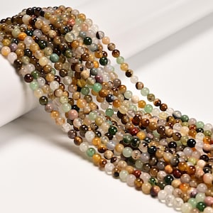 May include: Strands of gemstone beads in various colors, including brown, green, white, and yellow. The beads are round and appear to be strung together, suitable for jewelry making or crafting projects. The beads are on a white background.