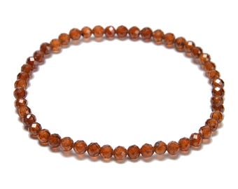 May include: A delicate bracelet featuring small, faceted, reddish-brown beads. The beads are strung together to form a circular shape, suitable for wrist wear. The bracelet is set against a plain white background.