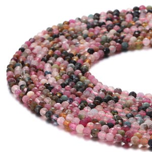 May include: A strand of multi-colored round gemstone beads. The beads are a mix of pink, green, blue, and brown. The beads are faceted and have a shiny finish.