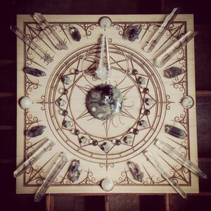 May include: A wooden board with a circular design featuring a large, gray and white stone in the center. The board is surrounded by a variety of clear quartz crystals and smaller stones.