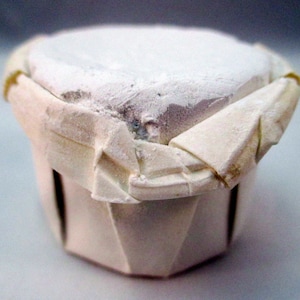 May include: A white chalk block wrapped in white paper. The paper is folded and creased, giving the block a unique shape.