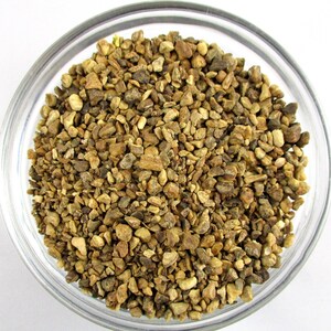 May include: A close-up view of a bowl filled with dried ginger pieces. The ginger pieces are a light brown color and have a rough texture.