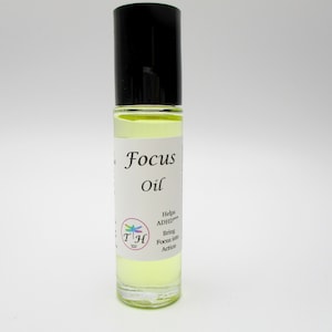 May include: A clear glass roll-on bottle with a black cap filled with yellow liquid. The label reads "Focus Oil" and includes the text "Helps ADHD", "Bring Focus into Action", and a colorful dragonfly logo.